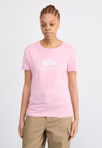 T-shirt en coton rose à manches courtes et col rond, avec un logo graphique blanc sur la poitrine. Design simple, coupe décontractée.
