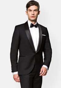 Czarny smoking z satynowymi szalowymi klapami, biała koszula i muszka. Charakteryzuje się dopasowanym krojem, zapięciem na jeden guzik oraz bocznymi kieszeniami.