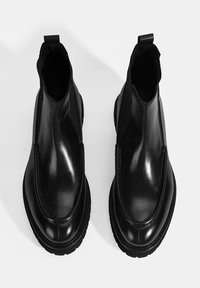 Bottines en cuir noir avec un design épuré, des panneaux élastiques sur les côtés et une semelle en caoutchouc robuste. Équipées d'une languette à l'arrière pour un enfilage facile.