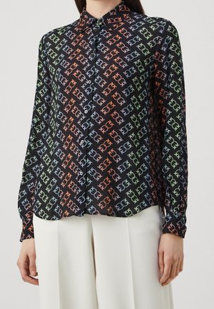 Czarna bluzka na guziki z długimi rękawami, zdobiona wzorem powtarzających się kolorowych geometrycznych łańcuchów, noszona z białymi spodniami z wysokim stanem.