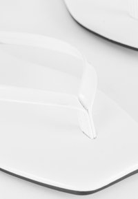 Witte flip-flops met een platte zool en zachte rubberen banden. Het ontwerp is minimalistisch met een gladde textuur en afgeronde randen.