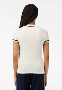 Camiseta de manga corta, ajustada, de color crema con acentos de canalé azul marino en los puños y el cuello, hecha de una tela suave y elástica.