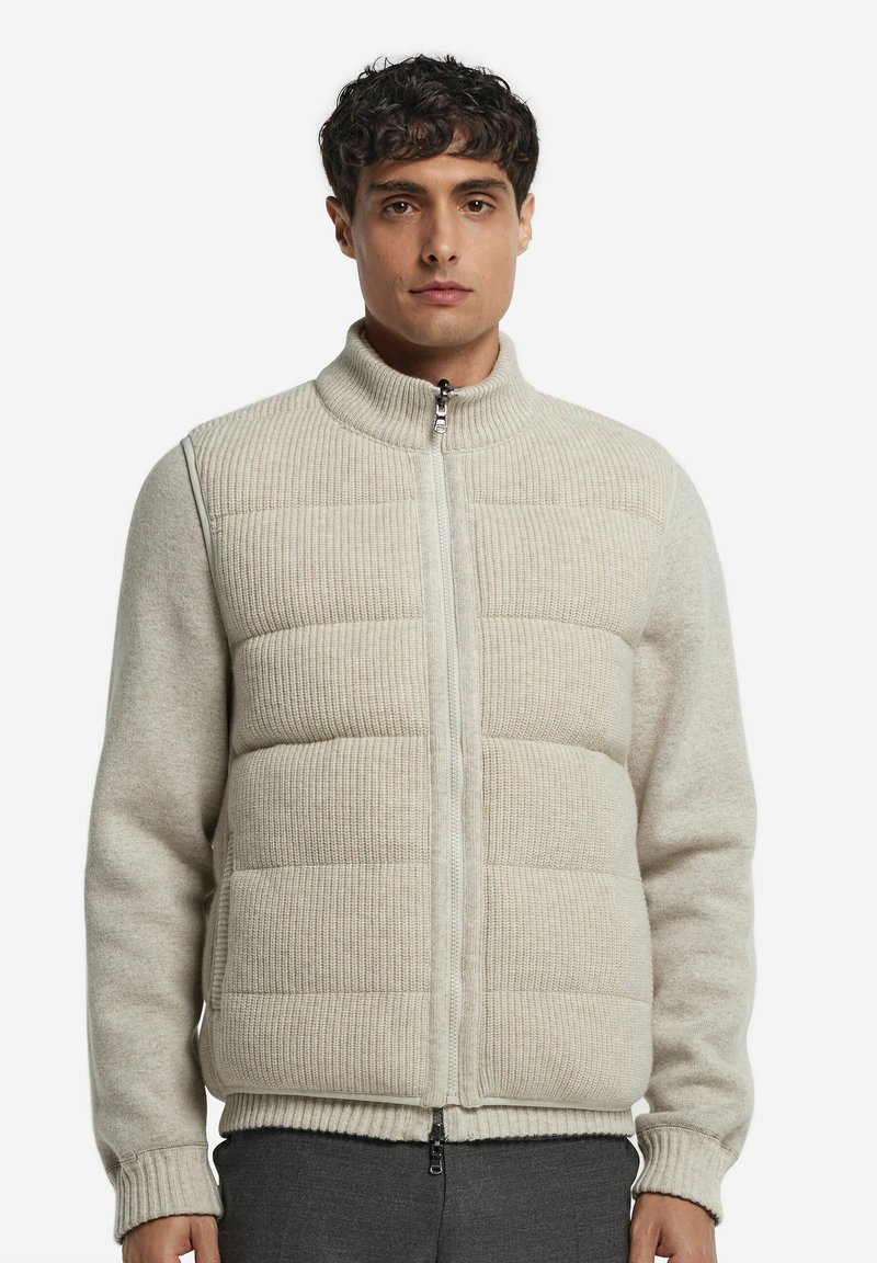 Beige Strickjacke mit einem Reißverschluss auf der Vorderseite, gerippter Textur an Schultern und Hals und gepolsterten, gesteppte Abschnitten am Körper. Normale Passform, hoher Kragen.