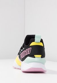 Baskets noires de sport avec une tige en mesh, des accents jaune, menthe et rose, et un logo "PUMA" rose bien en vue sur le talon. Semelle en caoutchouc.