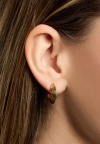 Metallringörhänge med en polerad guldfinish, med en strukturerad spiraldesign, säkert placerad i ett piercat öra.