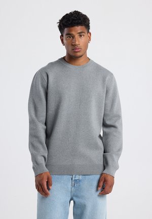 Sudadera gris de gran tamaño con un cuello redondo acanalado, mangas largas y puños y dobladillo acanalados, combinada con jeans de mezclilla azul claro.