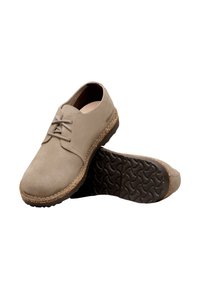 Bež semiš čevlji z okrogelim prstom, minimalnim vezanjem in teksturiranim gumijastim podplatom. Imajo pluto kot poudarek okoli roba podplata.