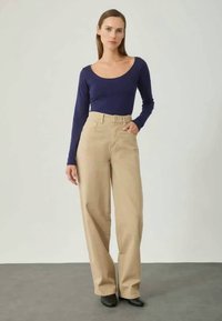 Navy long-sleeve top paired with high-waisted beige wide-leg pants, featuring a smooth texture and a relaxed fit. Black heeled shoes.