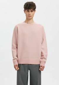 Lichtroze gebreide trui met een ronde hals en lange mouwen, voorzien van geribbelde manchetten en zoom. Gecombineerd met grijze, op maat gemaakte broek.