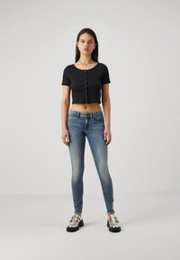 Juodas trumpas rankovėmis apkarpytas topas su mygtuko detale, derinamas su šviesiai mėlynomis liesomis džinsais ir metaliniais platforminiais batais.