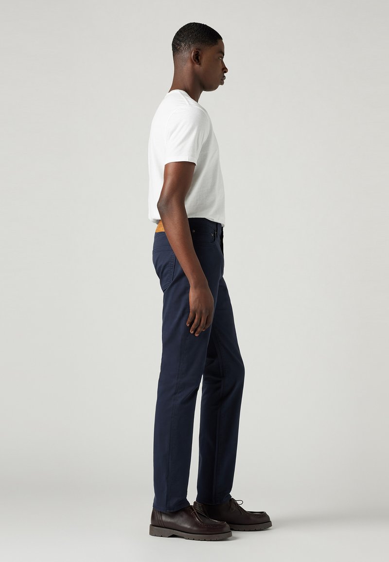 Camiseta blanca de manga corta combinada con pantalones chinos en color marino, con una textura suave, corte recto y zapatos de cuero marrón con suelas gruesas.