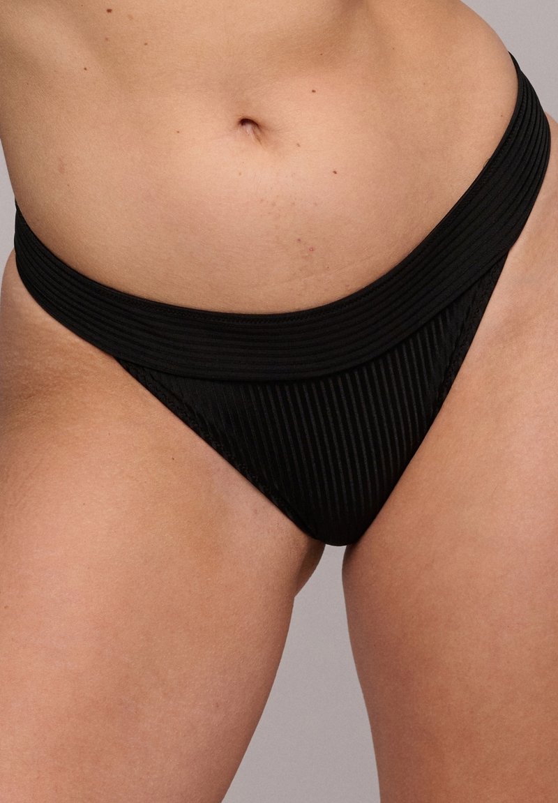 Slip bikini nero con una texture a coste, caratterizzato da un ampio elastico in vita e una linea di gamba alta, che enfatizza una copertura minima.