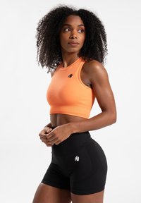 Oranje geribbelde sportcrop top gecombineerd met hoge zwarte shorts met een textuurpatroon en een wit logo aan de zijkant.