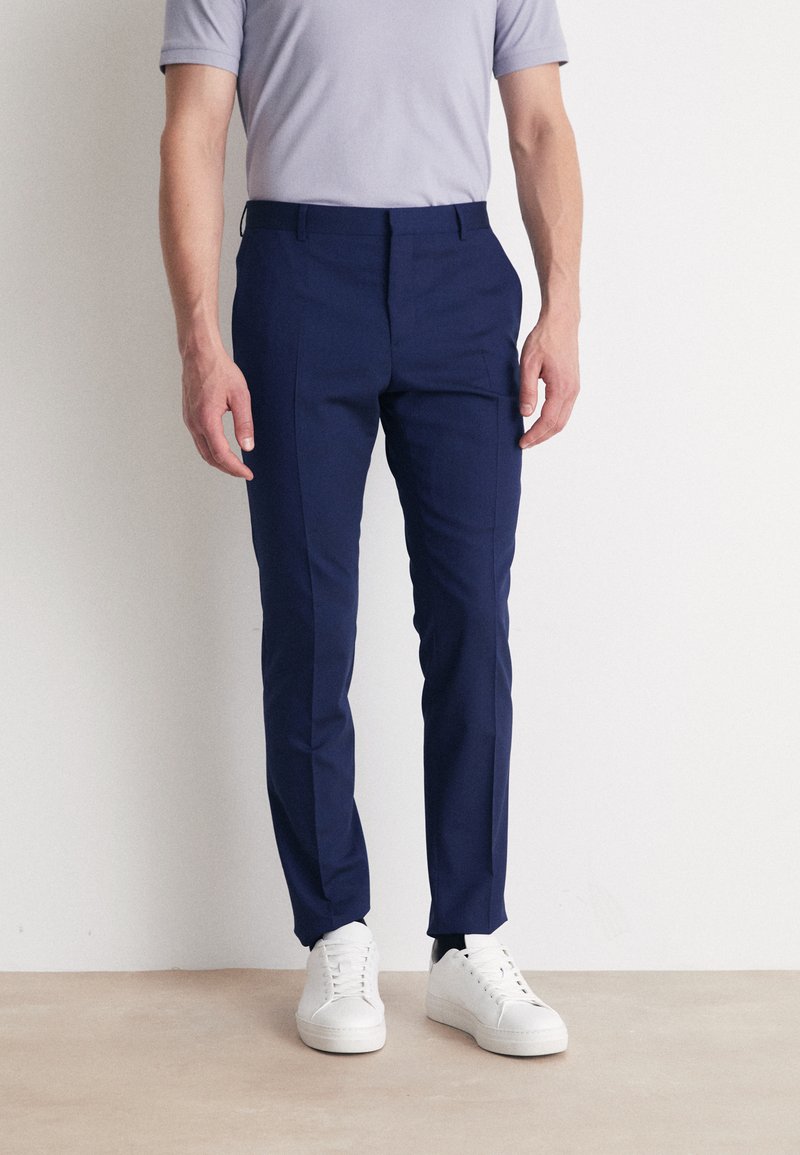 Merenpintaiset slim fit -housut, valmistettu liukkaasta kankaasta. Omistaa sivutaskut, vyölenkit ja on yhdistetty valkoisiin tennareihin.
