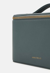 Teal synthetic leather bag with textured surface, gold zipper, and embossed brand logo, featuring a structured rectangular shape.