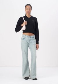 Black knitted cropped sweater with heart detail, paired with light blue flared jeans and a small pink handbag, featuring a smooth texture.