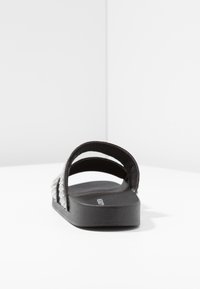 Sandales noires à glissière avec deux larges sangles, ornées d'accents en clous argentés. Semelle plate avec une texture mate, adaptées pour un usage décontracté.