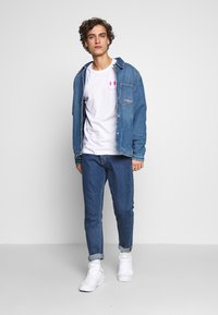 Denim jacket over a white t-shirt with pink smiley face, paired with blue jeans and white sneakers. Casual, layered outfit with contrast colors.