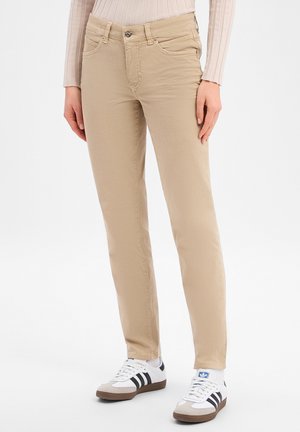 Beige rechte broek gedragen met witte Adidas sneakers met zwarte strepen, gemodelleerd door een persoon in een licht geribd shirt met lange mouwen.
