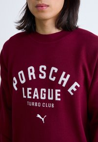 Bordeaux sweatshirt med hvid tekst: "PORSCH LEAGUE TURBO CLUB" og et lille hvidt Puma-logo. Blød, strikket tekstur og rund halsudskæring.