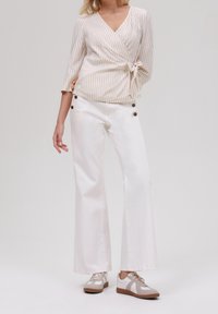 Bílé široké kalhoty s knoflíkovými detaily, které jsou kombinovány s lehkým béžovým pruhovaným topem s tříčtvrtečními rukávy a zavázaným pasem.