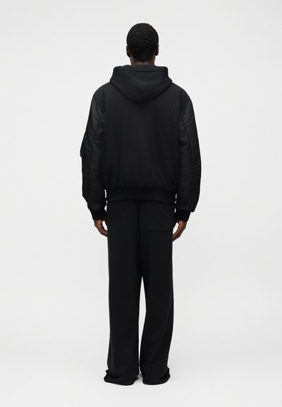 Μαύρο φούτερ με κουκούλα και πλαϊνά μανίκια με καπιτονέ ραφές, ριμπ μανσέτες και τελείωμα· συνδυασμένο με άνετο μαύρο παντελόνι. Απλός σχεδιασμός, απαλό ύφασμα και ομοιόμορφο χρώμα.