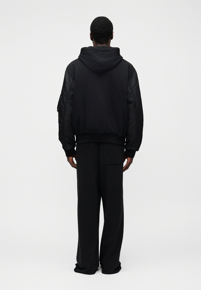 Sort hættetrøje med quiltede ærmer, ribstrikkede manchetter og kant; kombineret med løse sorte bukser. Simpelt design, blød tekstur og ensartet farve.