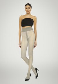 Beige gennemsigtige strømpebukser med høj talje i en glat finish, parret med en sort stropløs top og sorte høje hæle.