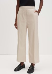 Beige wijde broek met een gladde textuur en zijzakken, voorzien van een platte tailleband. Gekoesterd met zwarte loafers.