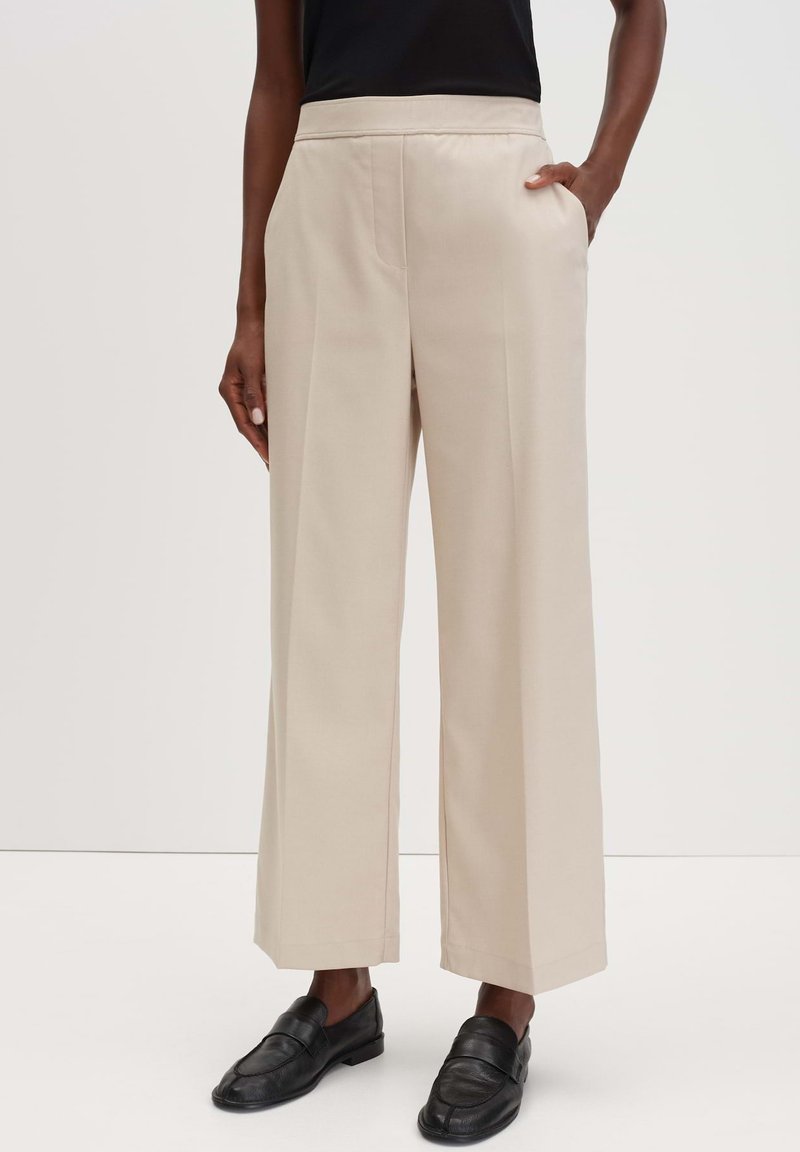 Beige wijde broek met een gladde textuur en zijzakken, voorzien van een platte tailleband. Gekoesterd met zwarte loafers.