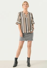 Stribet bluse i beige, sort og rustfarvet, korte ærmer, V-udskæring, parret med en slidset grå denimnederdel og sorte ankelstøvler.