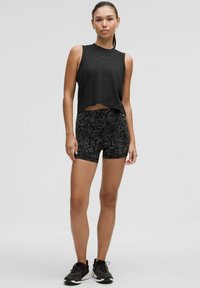 Top senza maniche nero con design cropped, abbinato a pantaloni corti high-waisted con un motivo leopardato nero. Scarpe sportive nere.