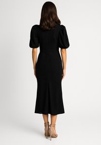 Czarna sukienka do połowy łydki z bufiastymi rękawami i fakturowaną tkaniną. Dopasowany krój podkreśla talię i delikatnie rozszerza się ku dołowi.