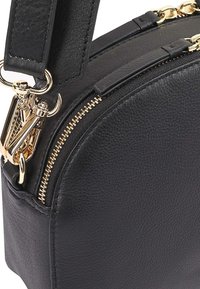 Zwarte leren handtas met een ronde vorm, voorzien van een gouden ritssluiting, metallic hardware en een afneembare schouderband. Textuurdetails op het oppervlak.