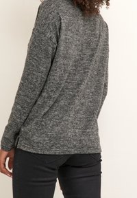 Pull en maille grise à coupe décontractée, avec une finition texturée, manches longues et fentes latérales à l'ourlet. Porté avec un pantalon noir.