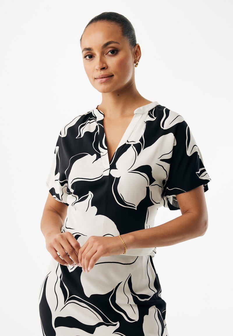 Schwarzweißes geblümtes Kleid mit kurzen Ärmeln, V-Ausschnitt und fließendem Stoff, mit einem auffälligen Blumenmuster und lockerem Schnitt.