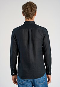 Camicia nera a maniche lunghe in tessuto di lino, con colletto, polsini con bottoni e orlo dritto, mostrata da dietro.