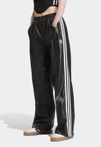 Svarta satinbyxor med elastisk midja, med tre vita ränder längs varje sida och en liten logotyp på underbenet.