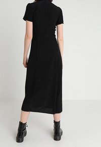 Černé midi šaty s krátkými rukávy, hladkým materiálem, přiléhavým živůtkem a mírně áčkovou sukní, v páru s černými kotníkovými botami.