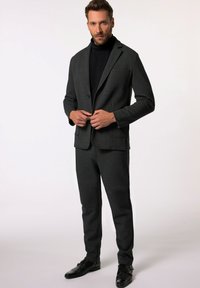 Traje gris oscuro hecho de una tela suave y texturizada. Presenta una chaqueta de un botón, pantalones ajustados y zapatos negros. Diseño simple y moderno.