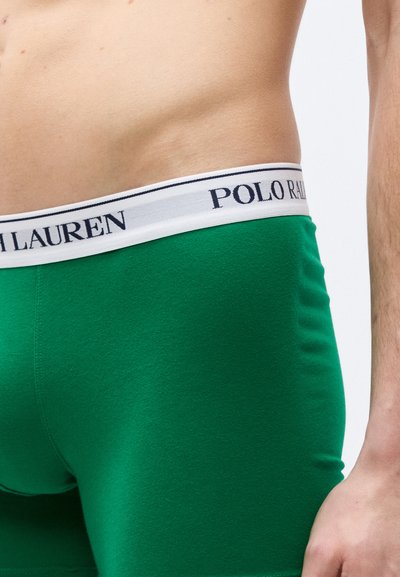Κοντινή λήψη ενός ατόμου που φοράει πράσινα ανδρικά εσώρουχα boxer μ ε λευκή μέση που φέρει την επωνυμία "Polo Ralph Lauren" στο ισχίο.