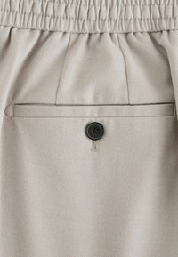 Beige Stoffshorts mit elastischem Bund, einer Gesäßtasche mit einem schwarzen Knopf und subtilen Nähdetails.