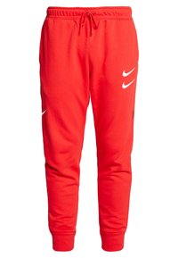 Röda mjukisbyxor i mjukt material med elastiskt midjeband och dragsko. Har två vita Nike-logotyper och smalnande ärmar.