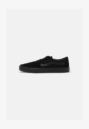 Black suede low-top sneakers with a textured finish, featuring black laces and a distinctive black rubber sole. Subtle red logo detail at the heel.