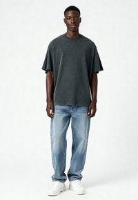 Tumši pelēks pārāk liels T-krekls ar īsām piedurknēm, apvienots ar gaiši ziliem taisniem džinsiem un baltām sporta apaviem. Gluda auduma, minimāla apdare.