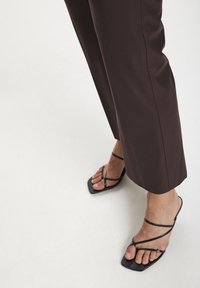 Svarta remsandaler med fyrkantiga tår som bärs med mörkbruna vida byxor. Släta ytor och minimalistiska designelement.