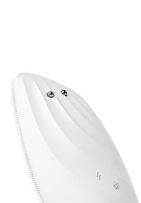 Vit enhet med en elegant, böjd design. Strukturerade silikonborstar på ena sidan, två metallknappar och minimal dekoration på ytan.