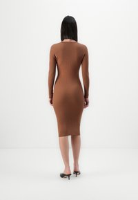 Vestido midi acastanhado com aros, de manga longa, design justo e decote redondo. Usado com sapatos de salto preto. Tecido simples e texturizado.