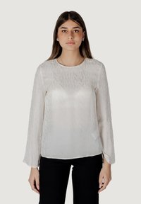 Blusa bianca trasparente a maniche lunghe con un sottile motivo testuale, scollo rotondo e spacchi laterali all'orlo, abbinata a pantaloni neri.