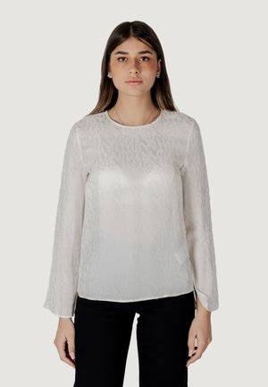 Blusa bianca trasparente a maniche lunghe con un sottile motivo testuale, scollo rotondo e spacchi laterali all'orlo, abbinata a pantaloni neri.
